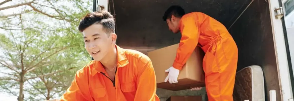 a group of men in orange jumpsuits carrying boxes